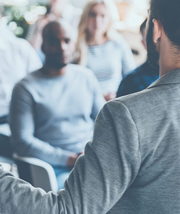The back of a man in a suit facing a crowd of people as he speaks. This symbolizes how sharing the expertise of your in-house experts can create brand awareness.