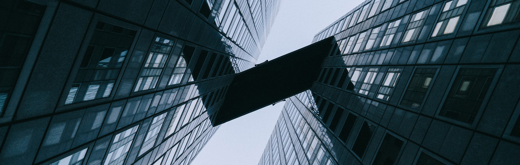 Looking straight up between 2 tall buildings with a bridge between the 2 buildings